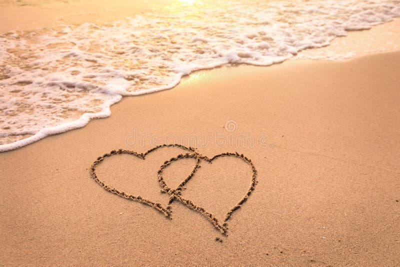 Romantic honeymoon holiday or Valentine`s day on the beach concept with two hearts drawn on the sand, tropical getaway for couples, love symbol