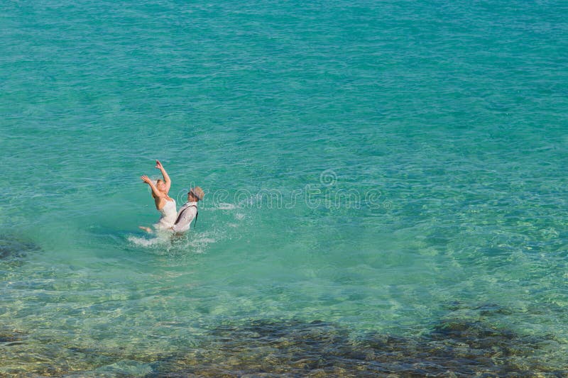 Romantic newly-married couple enjoying a summer vacation. Young groom lifting his bride in sea. royalty free stock image Romantic newly-married couple enjoying a summer vacation. Young groom lifting his bride in sea. royalty free stock image