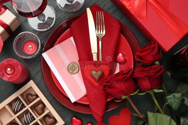 Romantic place setting with red roses on black table, flat lay. Valentine\ s day celebration