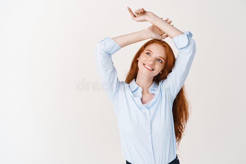 Romantic redhead girl smiling, raising hands up and looking dreamy at upper left corner, fantasizing something, standing