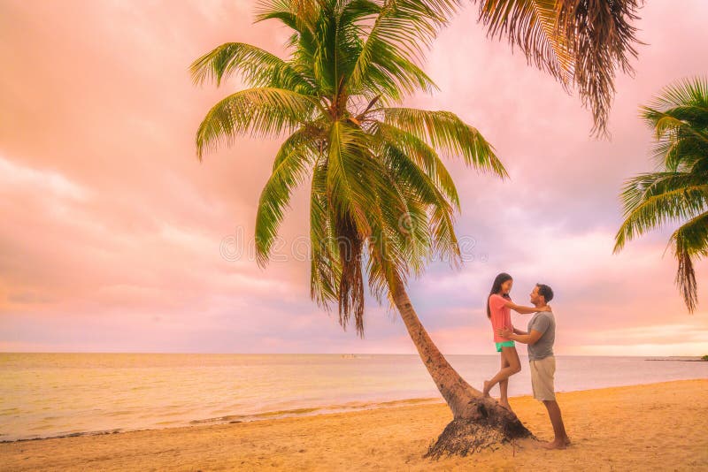 Romantic sunset stroll young couple in love embracing on palm trees at pink dusk clouds sky. Romance on summer travel vacation