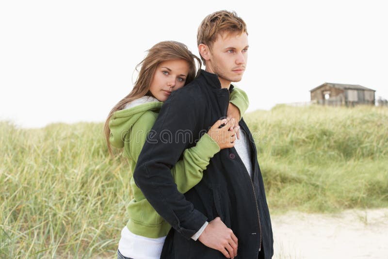 Romantic Young Couple Standing By Dunes With Beach Hut In Distance