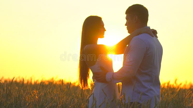 Romantic young happy couple silhouette in golden wheat field at sunset. Woman and man hugging and kissing against