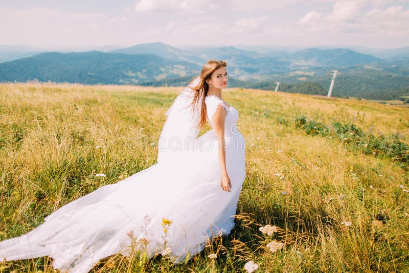 Romantic young pretty bride posing on the windy golden autumn field with small flowers. Hill landscape at background royalty free stock images Romantic young pretty bride posing on the windy golden autumn field with small flowers. Hill landscape at background royalty free stock images