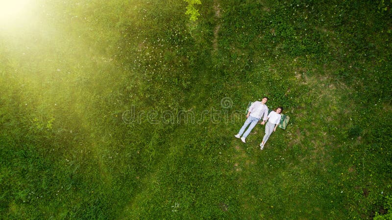Romantico nelle coppie di amore dei giovani che si trovano sull'erba in parco tenga per mano la vista da sopra fotografia stock libera da diritti Romantico nelle coppie di amore dei giovani che si trovano sull'erba in parco tenga per mano la vista da sopra fotografia stock libera da diritti