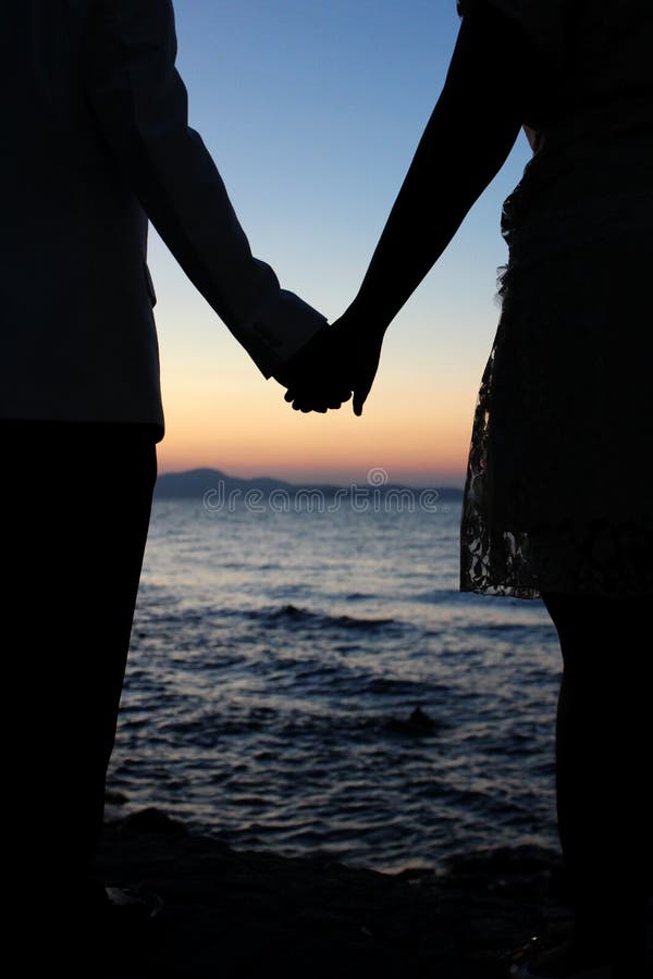 Romantische de holdingshanden van het silhouetpaar op een strand in zonsondergang stock foto Romantische de holdingshanden van het silhouetpaar op een strand in zonsondergang stock foto