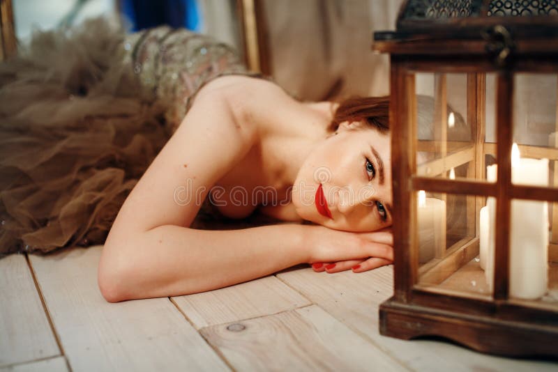 Romantische Frau, die auf einem Boden nahe Retro- Laterne mit Kerzen liegt