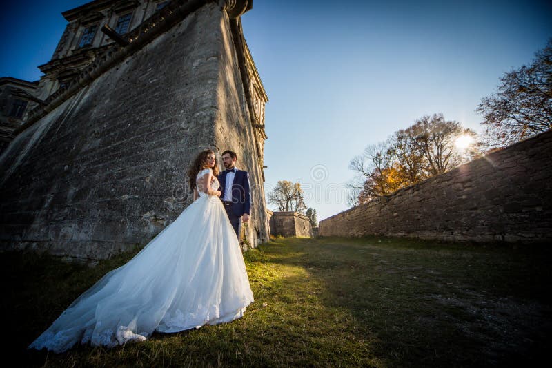 Romantische Märchenpaare von den Jungvermählten, die bei Sonnenuntergang nahe altem barockem Schloss aufwerfen stockbild Romantische Märchenpaare von den Jungvermählten, die bei Sonnenuntergang nahe altem barockem Schloss aufwerfen stockbild