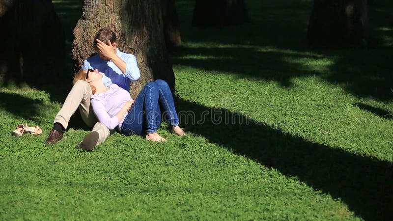 Romantische paarzitting onder een palm Een meisje op de overlapping van een kerel Een houdend van paar die in een park op het gra