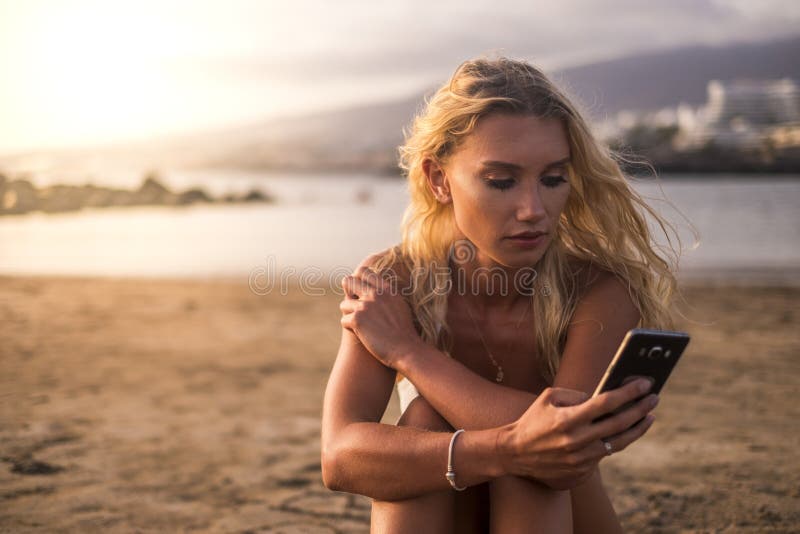 Romantisches schönes blondes junges Mädchen, welches das Telefon am Strand mit einem goldenen Sonnenuntergang in der Hintergrundb lizenzfreie stockbilder Romantisches schönes blondes junges Mädchen, welches das Telefon am Strand mit einem goldenen Sonnenuntergang in der Hintergrundb lizenzfreie stockbilder