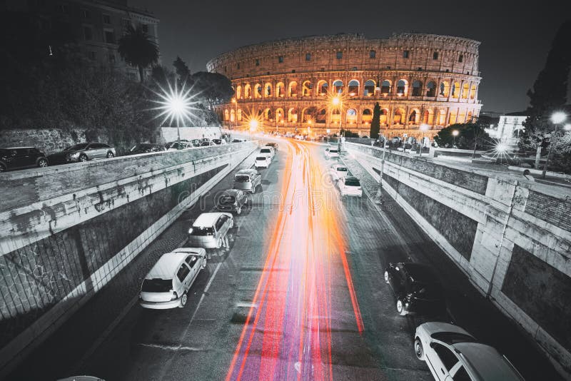 Rome, Italy. Colosseum Also Known As Flavian Amphitheatre In Evening Or Night Time. Night Traffic Light Trails Near