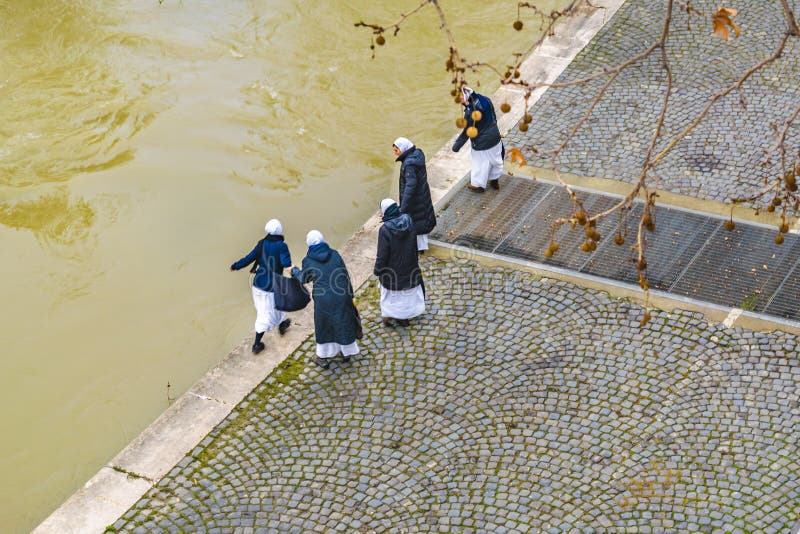 Nuns Walking at Tiber Walkway, Rome, Italy. ROME, ITALY, DECEMBER - 2017 - High angle shot 4 nuns walking at tiber cobblestone sidewalk at winter day in Rome stock photography Nuns Walking at Tiber Walkway, Rome, Italy. ROME, ITALY, DECEMBER - 2017 - High angle shot 4 nuns walking at tiber cobblestone sidewalk at winter day in Rome stock photography