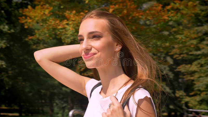 Rond loenst de jonge vrouw van Nice, het glimlachen, kruisenweg in park in dag in de zomer, horloge, gaat naar universiteit