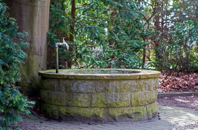 Ronde waterput met tapkraan in een begraafplaats met oude bomen stock afbeelding Ronde waterput met tapkraan in een begraafplaats met oude bomen stock afbeelding