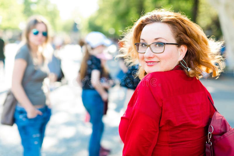 Roodharige vrouw die in rode blouse met glazen terug kijkt stock foto Roodharige vrouw die in rode blouse met glazen terug kijkt stock foto