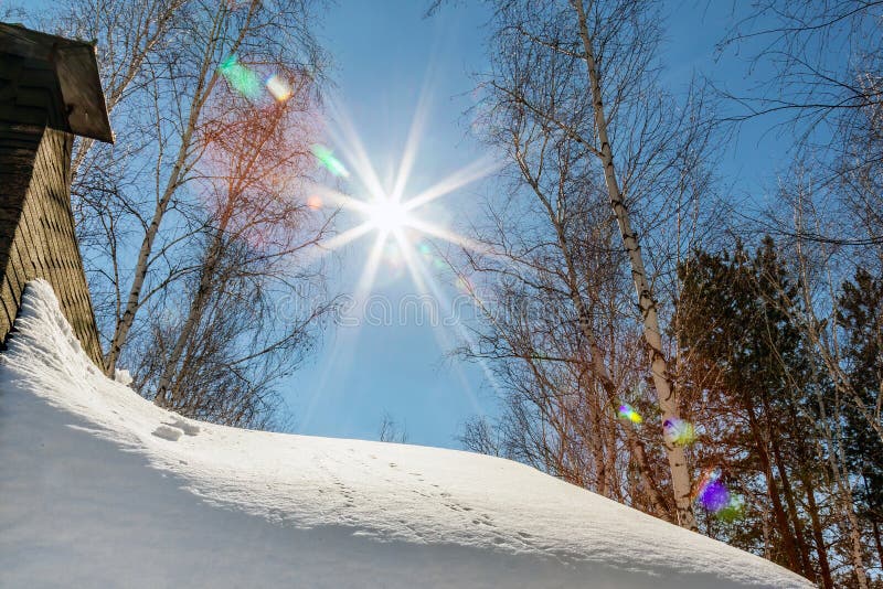 Roof of country cottage with chimney covered with big snow layer. Blue sky with sun flare on background. Rural house in royalty free stock photo Roof of country cottage with chimney covered with big snow layer. Blue sky with sun flare on background. Rural house in royalty free stock photo