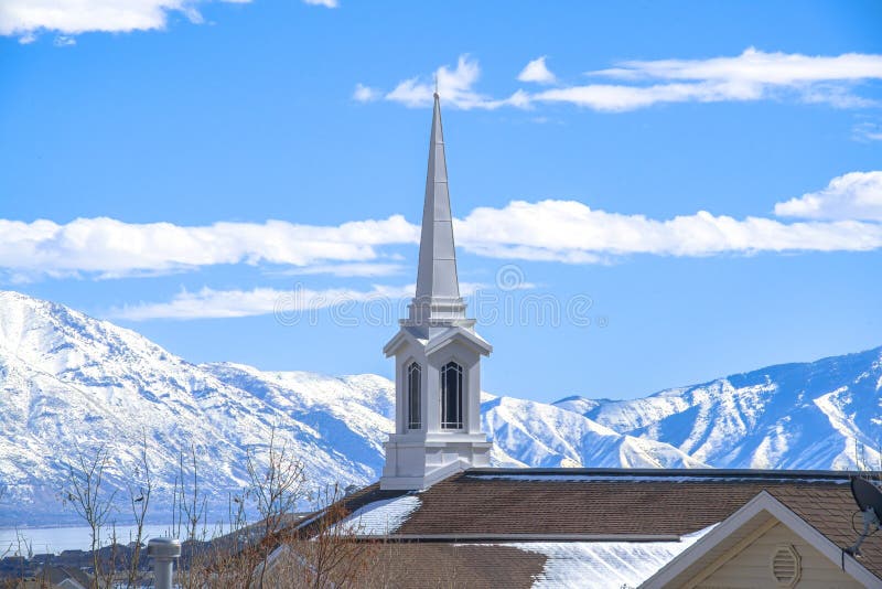 Rooftop of church with a modern spire design against snowy mountain and lake