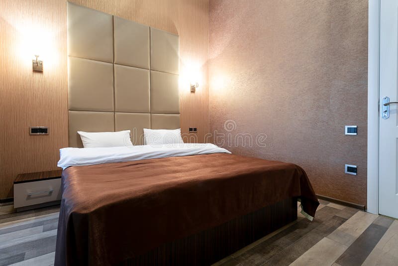 Room with a double bed, bedside table, and a white door, gray walls and laminate flooring. On each side of the bed on the wall lam stock photos Room with a double bed, bedside table, and a white door, gray walls and laminate flooring. On each side of the bed on the wall lam stock photos
