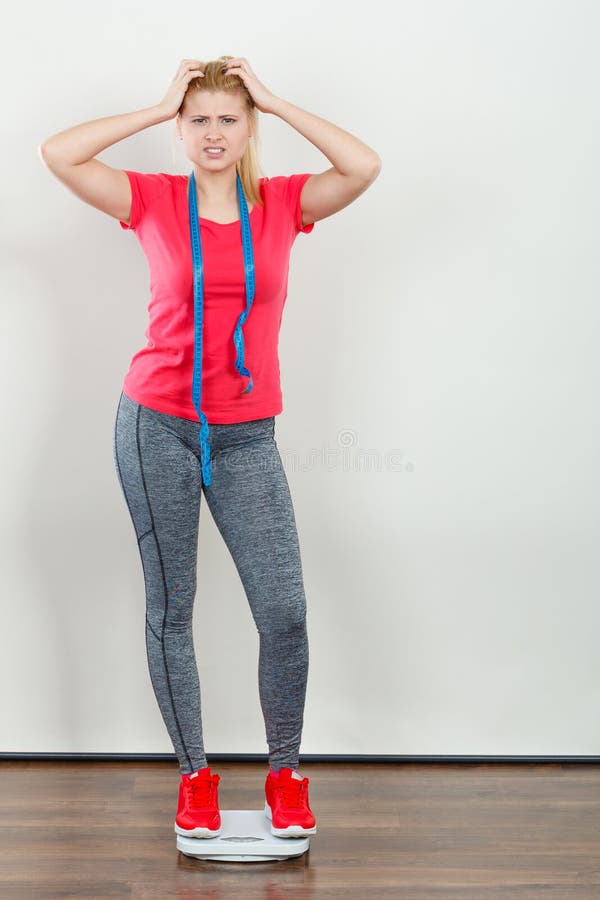 Ropa de deportes que lleva de la mujer que se coloca en la máquina del peso imagenes de archivo Ropa de deportes que lleva de la mujer que se coloca en la máquina del peso imagenes de archivo