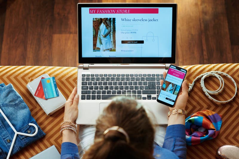 Ropa de la compra de la mujer mientras que tienda en línea en el ordenador portátil y el smartphone imagen de archivo Ropa de la compra de la mujer mientras que tienda en línea en el ordenador portátil y el smartphone imagen de archivo