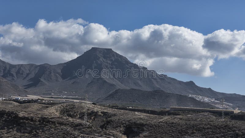 Roque del Conde com sua cimeira lisa, sob a luz solar bonita da manhã, vistas da vila pequena elegante do La Caleta, Te imagens de stock Roque del Conde com sua cimeira lisa, sob a luz solar bonita da manhã, vistas da vila pequena elegante do La Caleta, Te imagens de stock