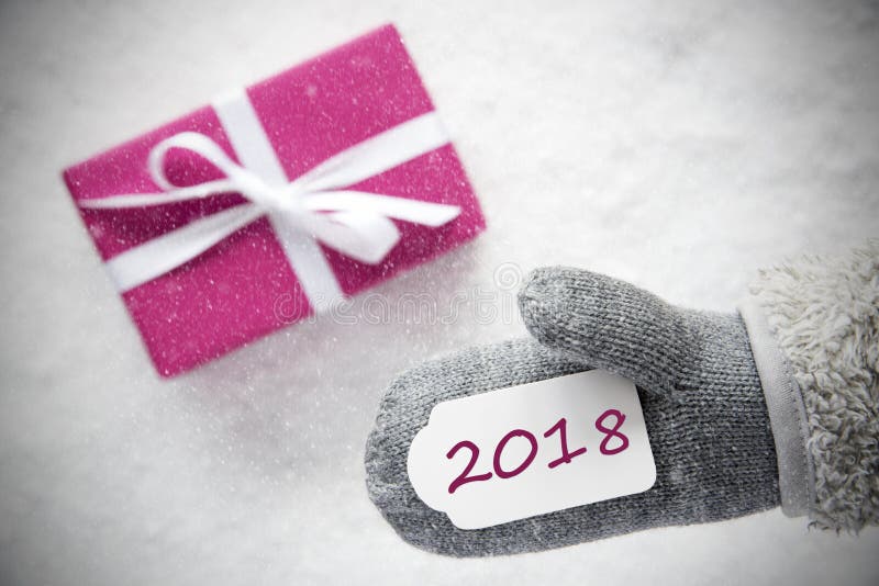Glove With Label With Text 2018 For Happy New Year. Pink Or Rose Gift Or Present On Snow In Background. Seasonal Greeting Card With Snowflakes. Glove With Label With Text 2018 For Happy New Year. Pink Or Rose Gift Or Present On Snow In Background. Seasonal Greeting Card With Snowflakes.