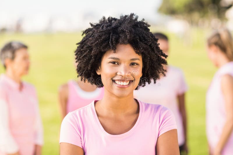 Rosa que lleva sonriente de la mujer joven para el cáncer de pecho delante de amigos foto de archivo libre de regalías Rosa que lleva sonriente de la mujer joven para el cáncer de pecho delante de amigos foto de archivo libre de regalías
