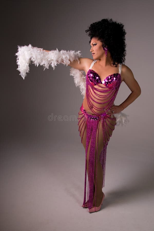 Full length shot of a glamorous Drag queen wearing a pink beaded showgirl costume, with a feather boa draped over her arm. Full length shot of a glamorous Drag queen wearing a pink beaded showgirl costume, with a feather boa draped over her arm.