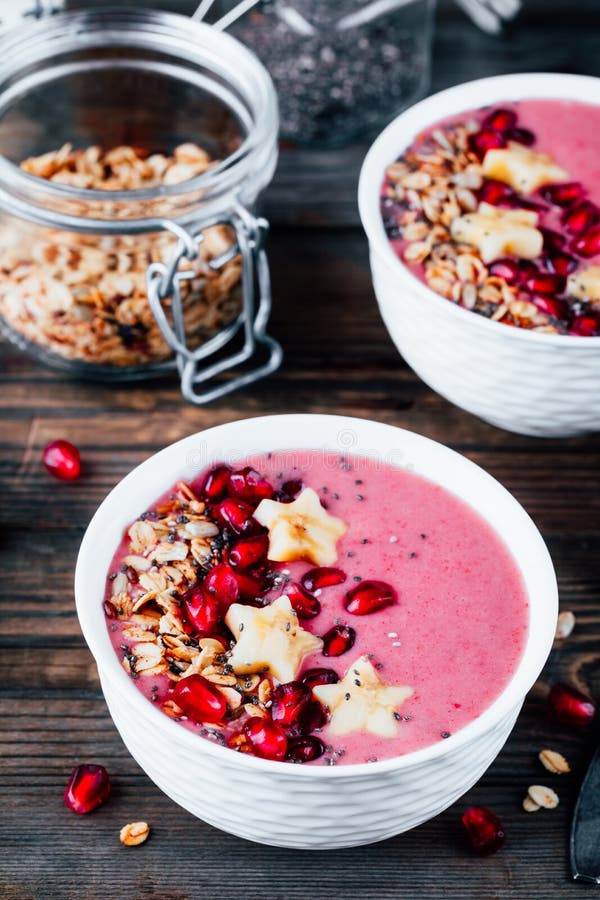Rosa smoothiebunke med granatäpplet, hemlagad granola, bananstjärnor och chiafrö royaltyfri bild Rosa smoothiebunke med granatäpplet, hemlagad granola, bananstjärnor och chiafrö royaltyfri bild