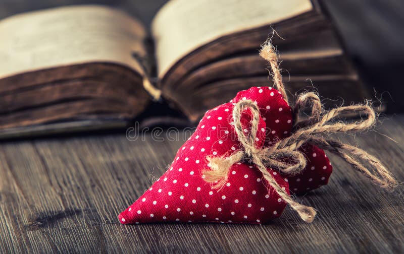 Valentines day. Red cloth handmade hearts on wooden background - table.Old book in background. Valentines day. Red cloth handmade hearts on wooden background - table.Old book in background