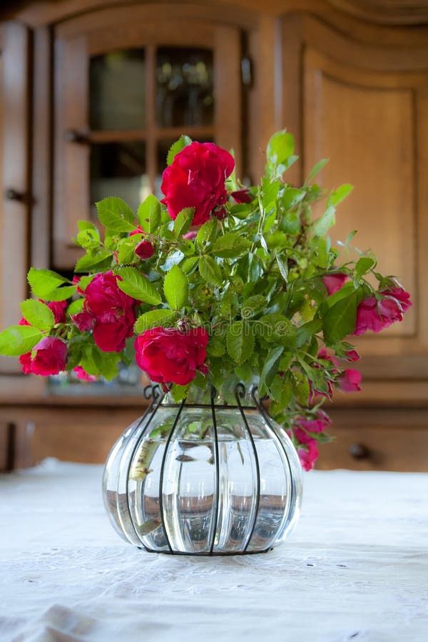 Garden bouquet of red roses in a glass, crystal, interesting vase with a wooden wardrobe in the background. Garden bouquet of red roses in a glass, crystal, interesting vase with a wooden wardrobe in the background