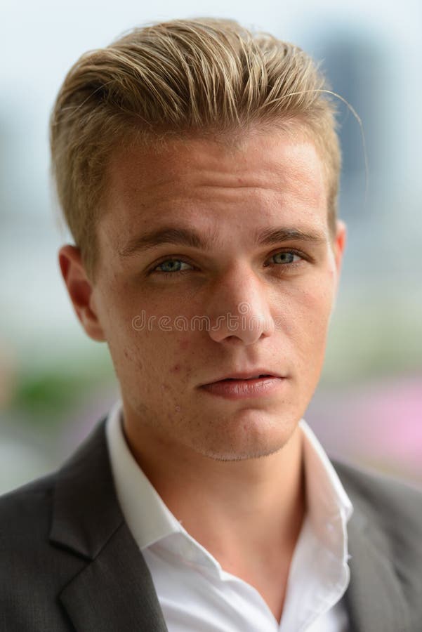 Vista de perfil de um homem bonito com cabelo loiro olhando para a câmera  ao ar livre