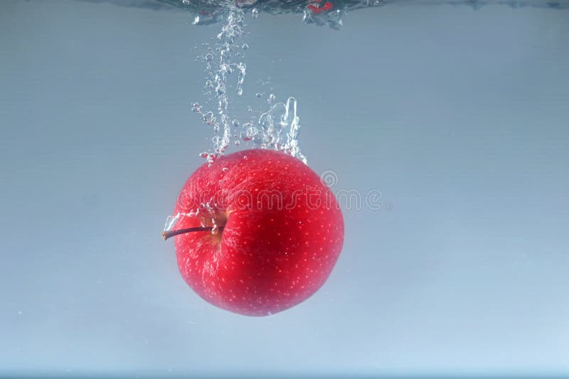 Rotapfel auf hellem Hintergrund ins Wasser fallen. Ein roter Apfel, der auf hellem Hintergrund ins Wasser fällt