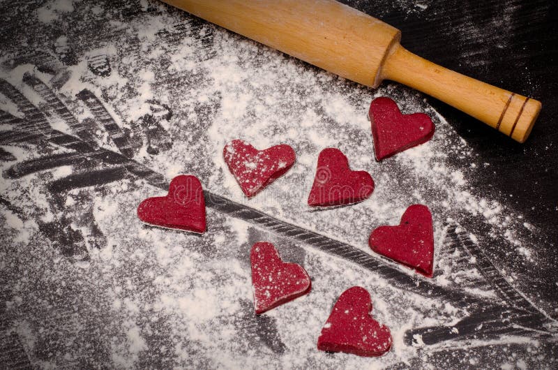 Rote Herzen gemacht vom Teig, vom hölzernen Nudelholz und von einem Pfeil gemalt auf Mehl lizenzfreies stockfoto Rote Herzen gemacht vom Teig, vom hölzernen Nudelholz und von einem Pfeil gemalt auf Mehl lizenzfreies stockfoto