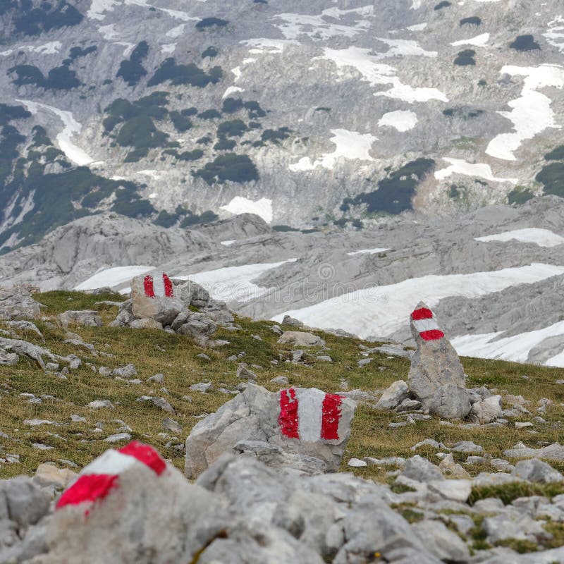 Rote Wandermarken auf Grassteinen mit Schnee und hohen Felsgebirgen im Hintergrund stockfotos Rote Wandermarken auf Grassteinen mit Schnee und hohen Felsgebirgen im Hintergrund stockfotos