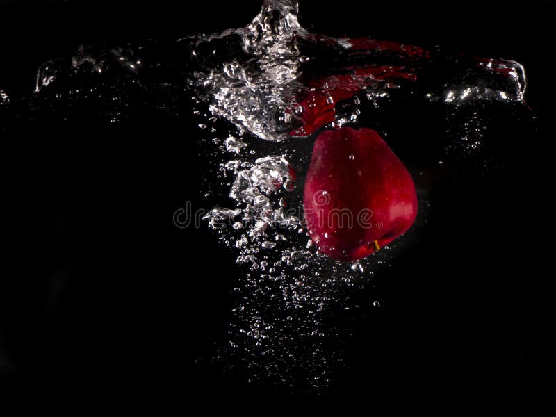 Roter Apfel, gelbe Zitrone, die in Spritzwasser auf schwarzem Hintergrund fällt stockfotos