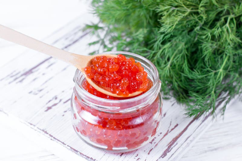 Roter Kaviar in einem Löffel über einem Glasgefäß auf weißem hölzernem Hintergrund lizenzfreies stockbild Roter Kaviar in einem Löffel über einem Glasgefäß auf weißem hölzernem Hintergrund lizenzfreies stockbild