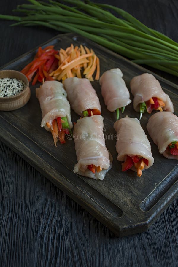 Rotoli casalinghi con il petto di pollo fresco con i verdi, fette della carota, peperone dolce su un tagliere scuro Il concetto d fotografia stock libera da diritti Rotoli casalinghi con il petto di pollo fresco con i verdi, fette della carota, peperone dolce su un tagliere scuro Il concetto d fotografia stock libera da diritti