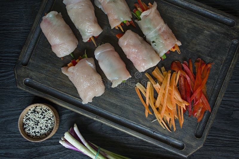 Rotoli casalinghi con il petto di pollo fresco con i verdi, fette della carota, peperone dolce su un tagliere scuro Il concetto d immagini stock libere da diritti Rotoli casalinghi con il petto di pollo fresco con i verdi, fette della carota, peperone dolce su un tagliere scuro Il concetto d immagini stock libere da diritti