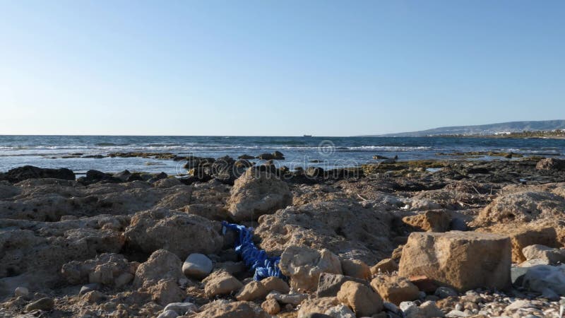 Rotsachtig die strand met plastic afval en afval wordt gevuld Schip en bergen op de achtergrond