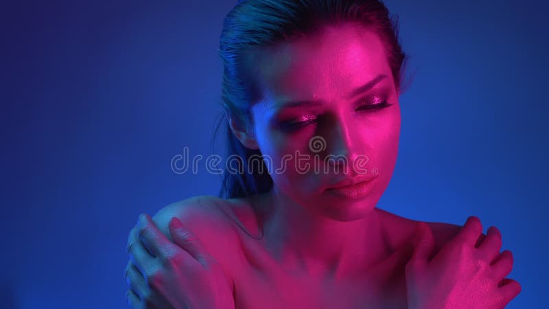 Rougeoyer modèle avec le maquillage de scintillement dans les lampes au néon bleues et roses observant à droite attentivement banque de vidéos Rougeoyer modèle avec le maquillage de scintillement dans les lampes au néon bleues et roses observant à droite attentivement banque de vidéos