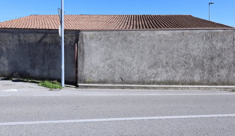 Rough concrete building with rooftiles on top at the roadside. Sidewalk and street in front stock images