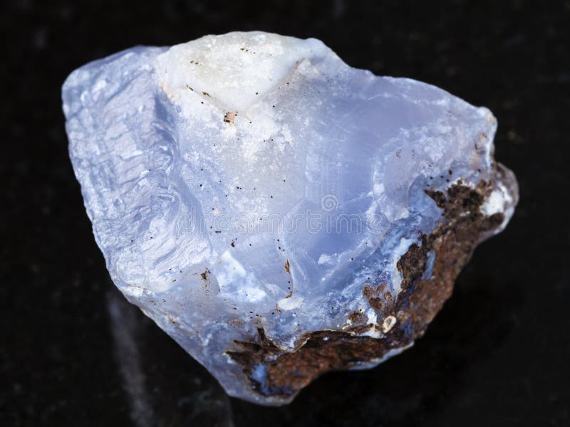 macro shooting of natural mineral rock specimen - rough crystal of blue Chalcedony gemstone on dark granite background from Transbaikalia (Zabaykalye), Russia