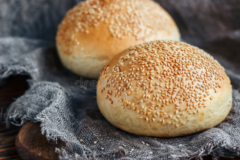 Round bun, sesame bun, bread rolls. Tasty burger bread with sesame on wooden, burlap background. Freshly baked hamburger buns. Top