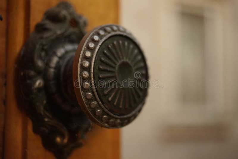 Round iron handle with a pattern on an old wooden door, closeup. Background in blur of a building with a window