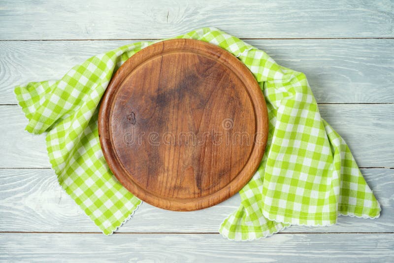 Round pizza board with green checked tablecloth on rustic wooden table .Kitchen, cooking or baking mock up background for design