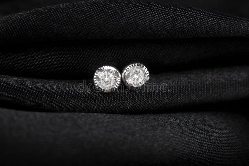 Round silver stud earrings with diamond on black fabric background