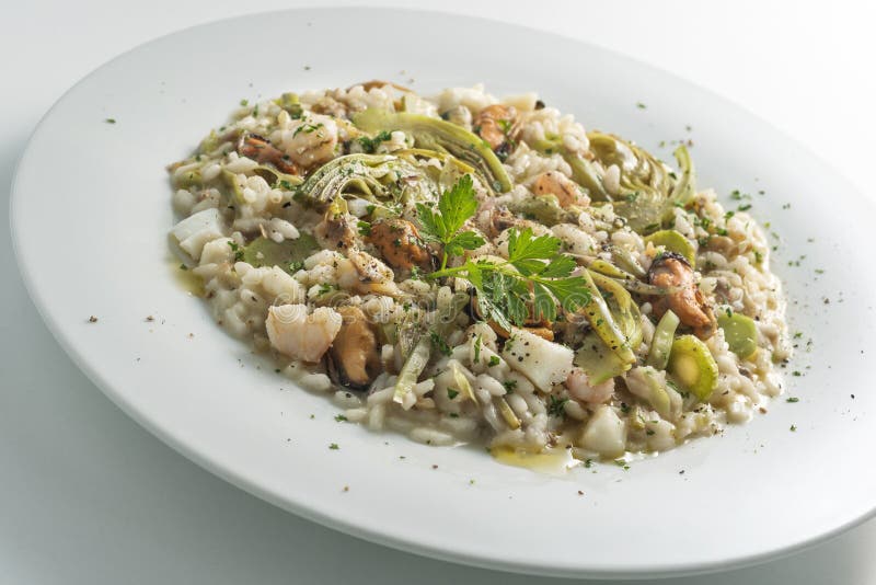 Round white dish of risotto with artichokes and seafood isolated on white background