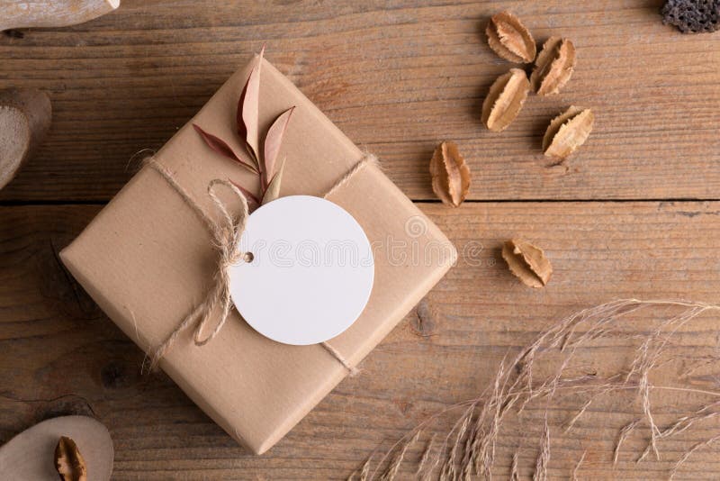 Round white gift tag mockup on craft wrapped presents on rustic wooden background with boho decoration