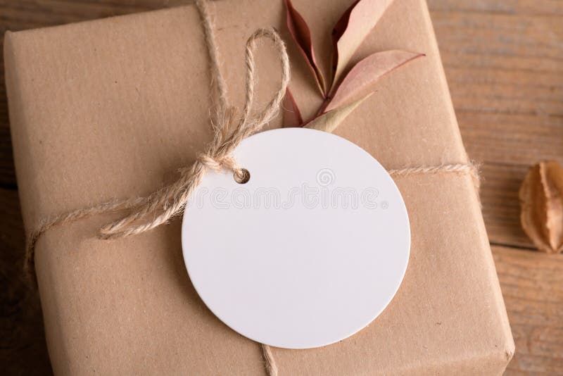 Round white gift tag mockup on craft wrapped presents on rustic wooden background with boho decoration